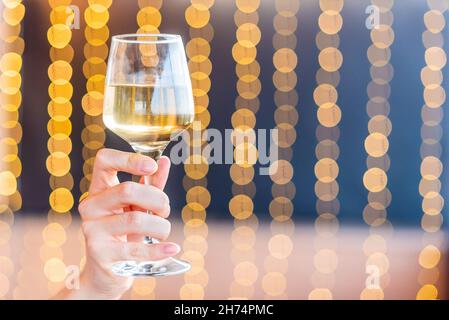 Hand holding a glass with white wine on blurred background Stock Photo