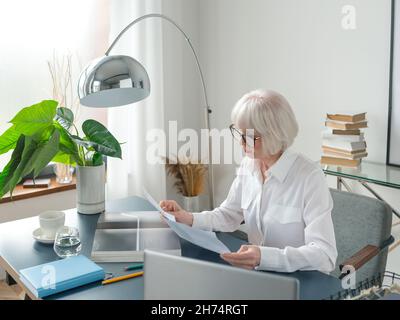 senior beautiful gray hair woman in white blouse reading documents in office. Work, senior people, issues, find a solution, experience concept Stock Photo