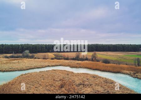 Aerial view of the countryside and frozen winding brook in the evening at sunset light. Beautiful nature landscape with cloudy sky Stock Photo