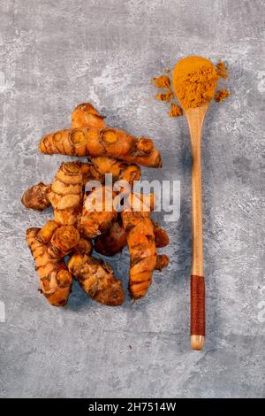 Ground Turmeric and Root Turmeric Arranged on a Grey Background Stock Photo