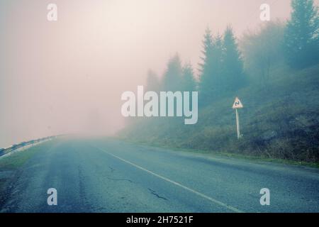 Car driving on a mountain road in foggy early morning Stock Photo