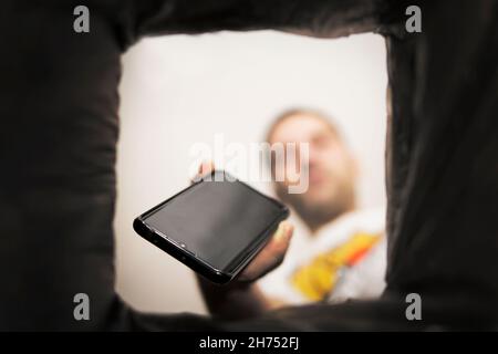 a man throws a non-working smartphone into a trash can. Bottom view from the trash can. The problem of recycling and pollution of the planet with garb Stock Photo