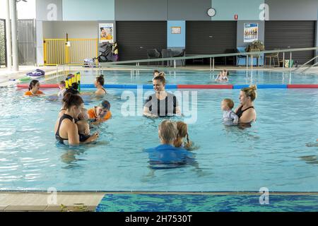 MACKAY, AUSTRALIA - Oct 22, 2021: Coaches in water giving babies swimming lessons with their parent