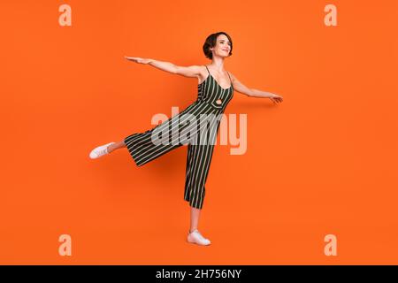 Full length profile photo of sweet brunette millennial lady pose wear overall sneakers isolated on orange background Stock Photo
