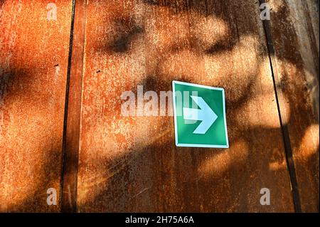 Green sign with a white arrow pointing to the right on a weathered wooden surface in the sun Stock Photo