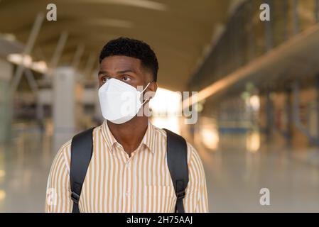 African man traveling and waiting at airport during covid and wearing face mask while social distancing Stock Photo