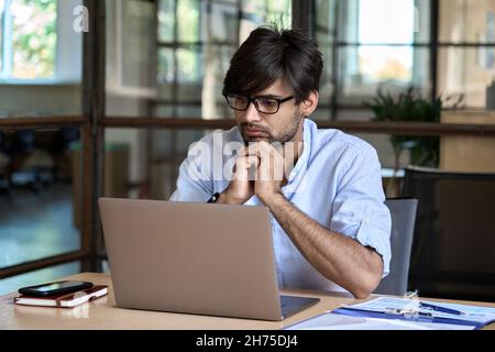 Young Indian business man watching business webinar on laptop in office. Stock Photo