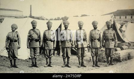 A historical view of seven British Colonial Indian infantry soldiers, standing at attention in a camp, c. 1902. Stock Photo