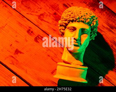 Gypsum copy of ancient statue Hermes head in orange green neon light. Neon image with ancient greek sculpture Hermes head. Minimal art fantasy concept Stock Photo