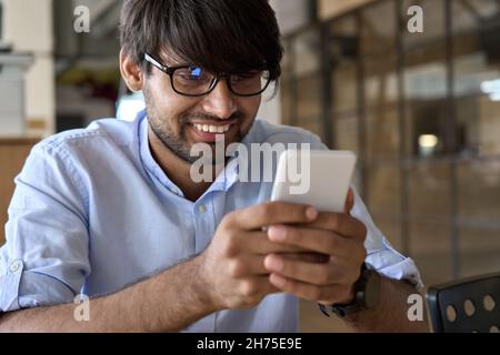 Happy Indian businessman using smartphone apps working in office. Stock Photo