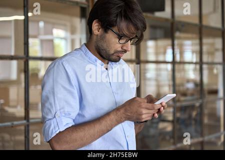 Young Indian business man using cellphone apps standing in office. Stock Photo
