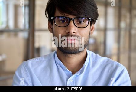 Headshot of young Indian businessman wears glasses looks at camera in office. Stock Photo
