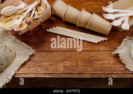 Different wooden kitchenware on wooden table. Wooden cutlery on old planks. Bamboo straws and disposable paper cups. Eco-friendly tableware. Zero wast Stock Photo