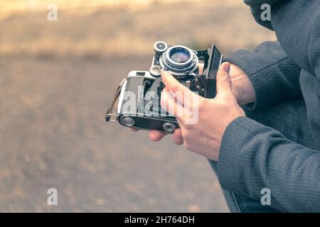 A man holds an antique, but working camera and adjusts it for photography on the street Stock Photo