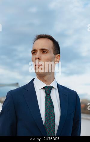 Young businessman in a suit and tie looking away thoughtful outside in a rooftop with a cloudy sky Stock Photo