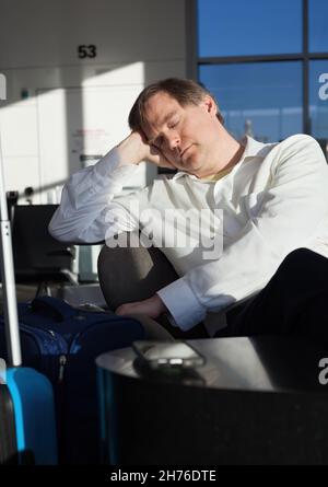Tired Caucasian businessman sleeping in airport terminal with luggage while waiting for flight Stock Photo