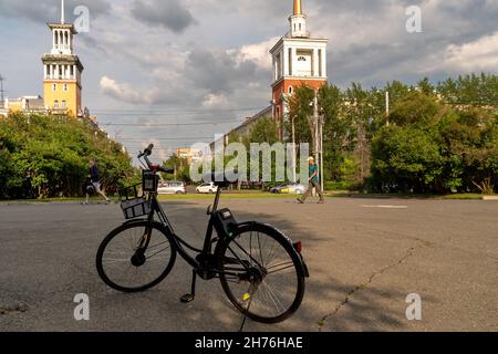 A bike for rent via the Internet app stands in the shade in a park against the backdrop of a city street on a summer day. Stock Photo