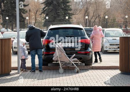 A young family with two children near a parked car in the parking lot on a spring sunny day. Stock Photo
