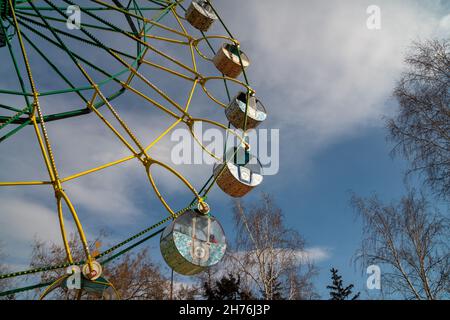 Part of a large Ferris wheel with painted cabins against the sky in a city amusement park. Stock Photo