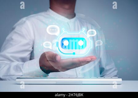 Digital chatbot concept. Virtual bot icon with speech bubbles symbol on hand while using computer for providing access to information and data online, Stock Photo
