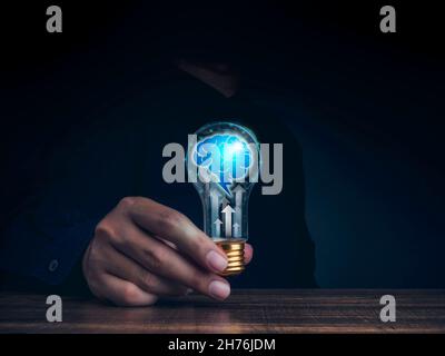 Creative, idea, innovation, knowledge, and inspiration concept. The human brain icon with rising arrows glowing inside the digital light bulb in man's Stock Photo
