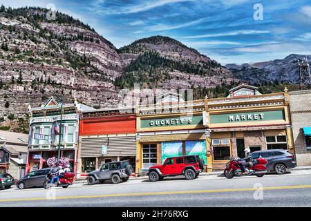 The historic downtown Main street with parked car and passing motorcycles with San Juan mountains in background - Ouray, Colorado, USA - October, 2021 Stock Photo