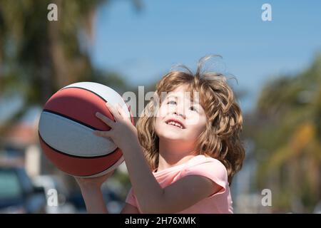 Cute smiling boy plays basketball. Active kids enjoying outdoor game with basket ball. Stock Photo