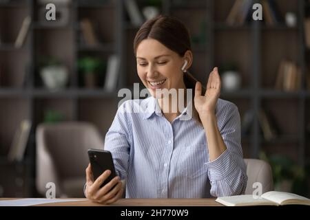 Young woman wear earphones holds smart phone use videocall Stock Photo