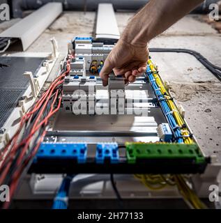 A male electrician works in a switchboard with an electrical connecting cable. Stock Photo