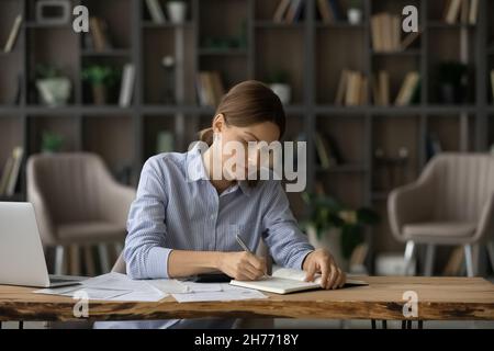 Woman writing in diary, jotting to-do list seated at desk Stock Photo