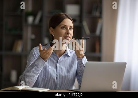 Attractive woman sit at desk holding smartphone talk on speakerphone Stock Photo