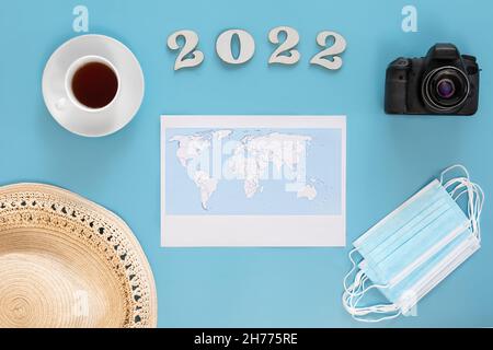 Travel flat lay composition with world map and numbers 2022 on blue background. Stock Photo