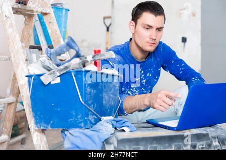 Male contractor with laptop in repairable apartment Stock Photo