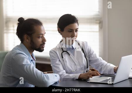 Indian woman doctor consulting African American patient, using laptop Stock Photo