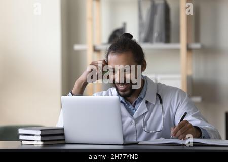 Smiling African American man doctor intern using laptop, taking notes Stock Photo