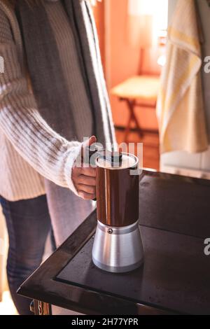 Woman making hot coffee drink with percolator at old stove in tourist hut Stock Photo