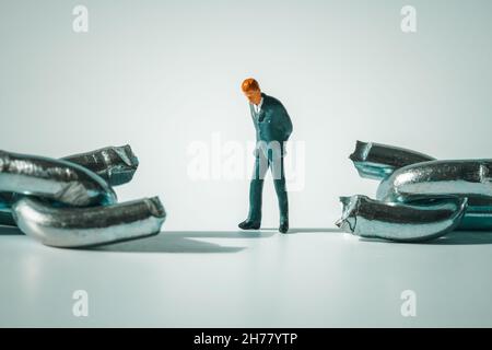 Macro photo of thoughtful businessman figurine standing between broken chain.  Sad and stressed miniature man close-up. Conflict, bankruptcy Stock Photo