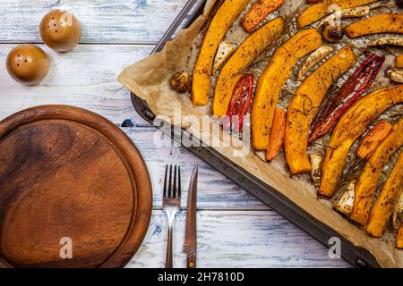 Baked pumpkin hokkaido and vegetable on wooden plate. Roasted vegetable as autumn dinner. Setting the dining table Stock Photo