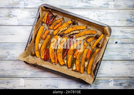 Baked pumpkin slices in baking tray on white wooden table Stock Photo