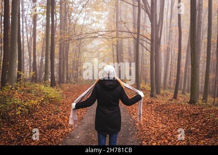 Woman ties woolen scarf during walk in autumn forest. Warm clothing in cold foggy morning Stock Photo