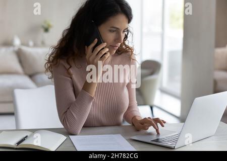 Close up confident businesswoman talking on phone and using laptop Stock Photo