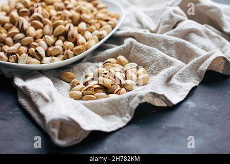 A plate with raw pistachios in a shell on a light tablecloth on a dark gray background Stock Photo