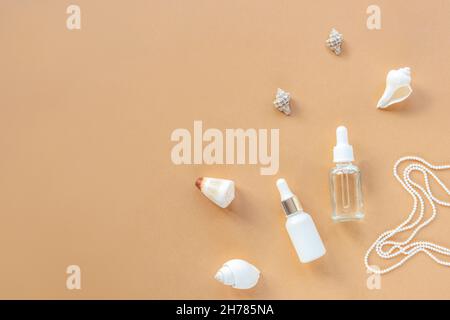 White serum bottles on beige background with seashells and pearl necklace. Natural cosmetics concept. Top view, flat lay, copy space. Stock Photo