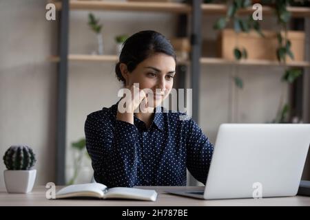 Happy pensive young Indian businesswoman working on computer. Stock Photo
