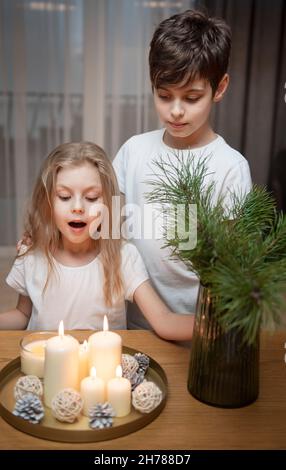 Cozy Christmas at home. Children - a boy and a girl blow out Christmas candles at home in the evening. Stock Photo