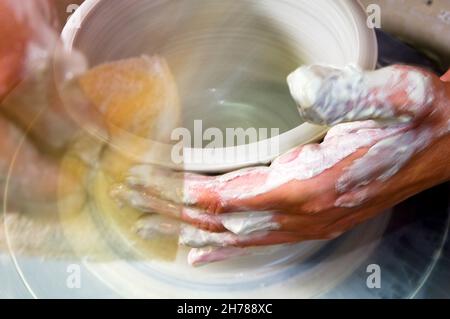 An European female potter in her workshop shapes clay on a potter's wheel. Closeup of her hands showing motion Stock Photo
