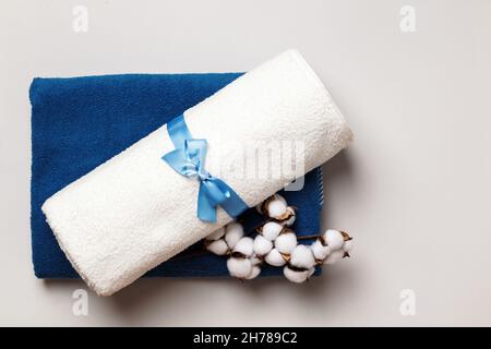 Rolled up white and blue terry towels with a cotton twig on a gray background. Stock Photo