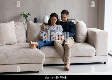 Couple relaxing on sofa in living room with digital tablet Stock Photo