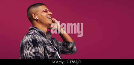 Young man enjoying his favourite songs. Happy young man playing music on his wireless earphones. Handsome young man smiling cheerfully while standing Stock Photo