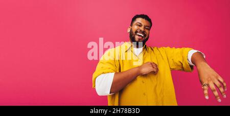 Ethnic man enjoying listening to his favourite music in a studio. Happy young man dancing while streaming music on wireless earphones. Smiling young m Stock Photo